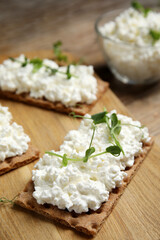 Obraz na płótnie Canvas Crispy crackers with cottage cheese and microgreens on wooden board, closeup
