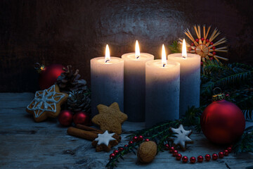 Four Advent candles with Christmas decoration, baubles and cookies on rustic wooden planks against...