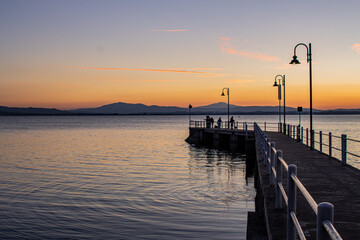 Lake with jetty at sunset. Relaxing Italian landscape at sunset in autumn. Trasimeno lake at sunset