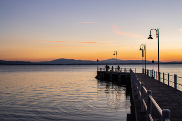Fototapeta premium Lake with jetty at sunset. Relaxing Italian landscape at sunset in autumn. Trasimeno lake at sunset