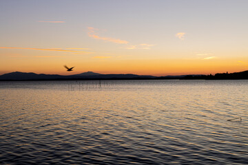 Obraz premium Lake with jetty at sunset. Relaxing Italian landscape at sunset in autumn. Trasimeno lake at sunset