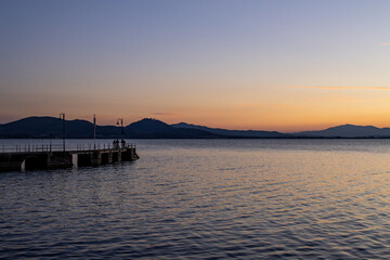 Fototapeta na wymiar Lake with jetty at sunset. Relaxing Italian landscape at sunset in autumn. Trasimeno lake at sunset
