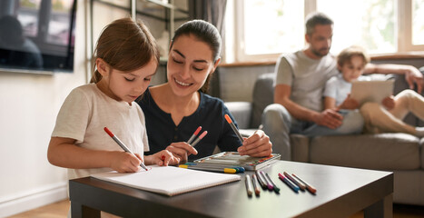 Smiling mom draw paint together with small daughter