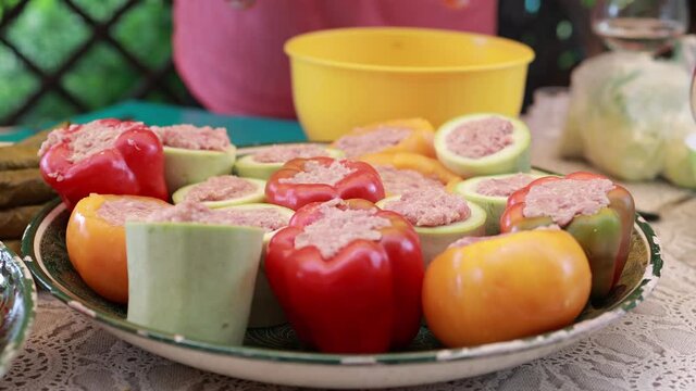 People hands are preparing food. Peppers, tomatoes, zucchini and grape leaves stuffed with minced meat.
