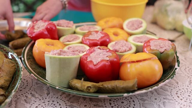 People hands are preparing food. Peppers, tomatoes, zucchini and grape leaves stuffed with minced meat.
