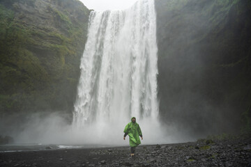Tourist man admiring of the wild nature while walking at the black beach with waterfall