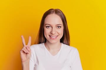 Photo of young cheerful woman happy positive smile show peace cool v-sign isolated over yellow color background