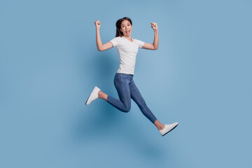 Fototapeta premium Portrait of energetic carefree excited lady jump run winner concept on blue background