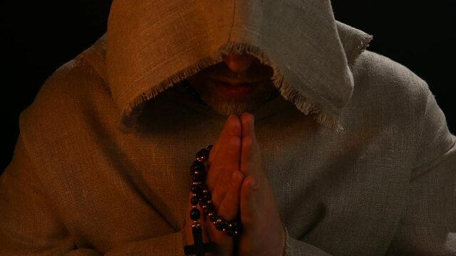 Monk in haircloth cowl robe praying in candlelight