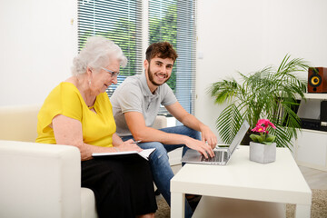 young man helping a old senior woman doing paperwork and administrative procedures with laptop...