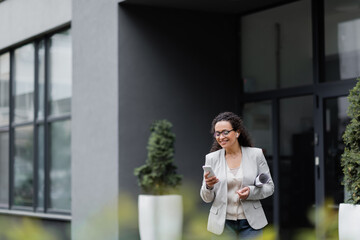 african american businesswoman with rolled papers smiling while using cellphone on blurred foreground outdoors