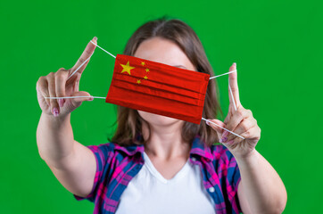 Woman in a plaid shirt holds a medical mask with of the China flag on a green background