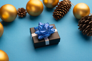 Little gift box with a blue ribbon, Christmas balls and cones on a light blue background