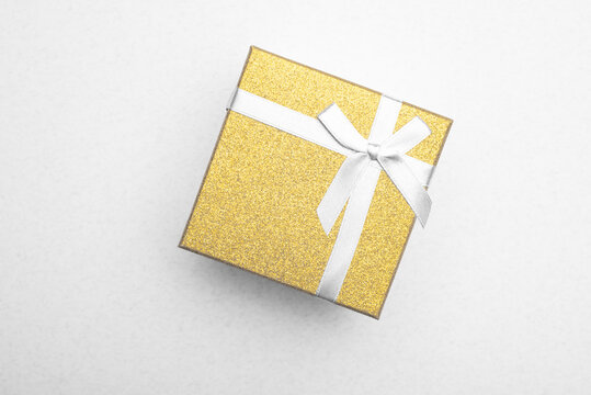 Gold gift box with a ribbon on a light background. Top view, flat lay. 