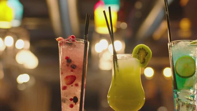 Professional barman decorates a cocktail with fruits. Bartender prepares many cocktails at the beautiful bar pub and serves a cocktail. Barman preparing colorful cocktails. Hand putting glas on table
