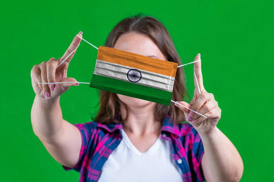 Woman in a plaid shirt holds a medical mask with of the India flag on a green background