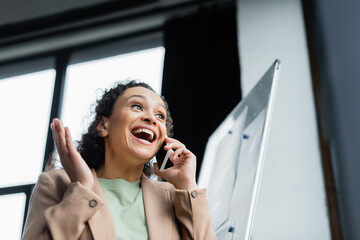 low angle view of amazed african american businesswoman talking on mobile phone in office