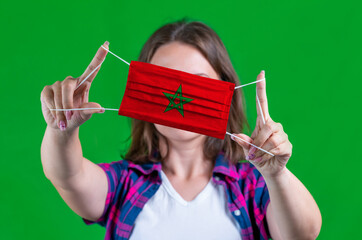 Woman in a plaid shirt holds a medical mask with of the Morocco flag on a green background