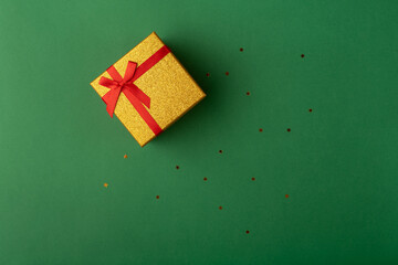 Red and gold gift box on a deep green background with golden stars. Flat lay, top view.