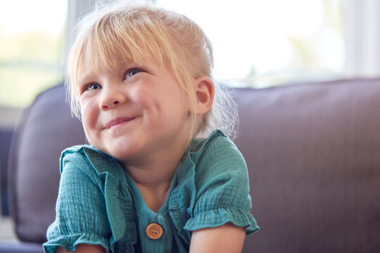 Smiling Young Girl Sitting On Sofa In Lounge At Home Watching TV