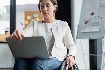 businesswoman in wheelchair looking at laptop while working in office