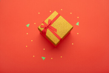 Red and gold gift box on a bright red background with golden stars and little Christmas trees.