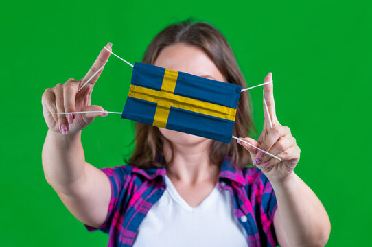 Woman in a plaid shirt holds a medical mask with of the Sweden flag on a green background
