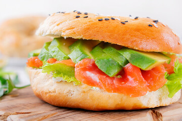 Bagel with salted trout, avocado, lettuce and cream cheese on the wooden board. Layered sandwich