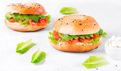 Bagel with salted trout, avocado, lettuce and cream cheese on the white table. Layered sandwich