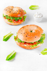 Bagel with salted trout, avocado, lettuce and cream cheese on the white table. Layered sandwich