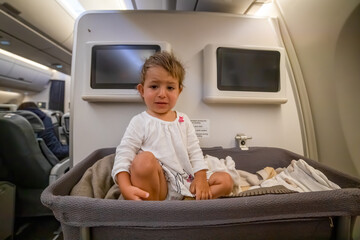 crying infant baby seat in a special cradle on the plane. Baby look at the side in bassinet On Airplane