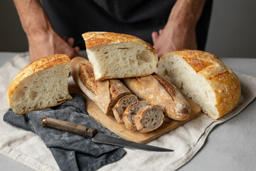 an adult European male baker holds a round fresh bread in his hands. a man in a bakery holds a yeast-free bread on sourdough and a baguette. cool and healthy bread for the whole family. vegan food for