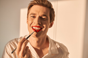 Bisexual ginger man preparing unique make up for himself while applying red lipstick