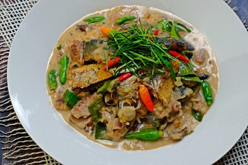 Stir fried mackerel with coconut milk in white plate on wooden table. Authentic Thai food.
