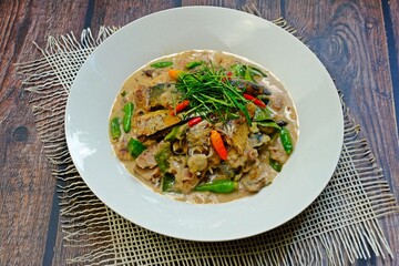 Stir fried mackerel with coconut milk in white plate on wooden table. Authentic Thai food.
