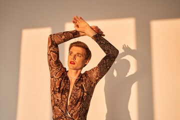 Man with drag queen makeup holding his hands up and looking away while posing