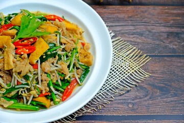Stir fried tofu with bean sprouts, green chives and minced pork in white plate on wooden table.