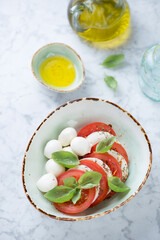 Bowl of italian traditional caprese salad over light-grey marble background, high angle view, studio shot