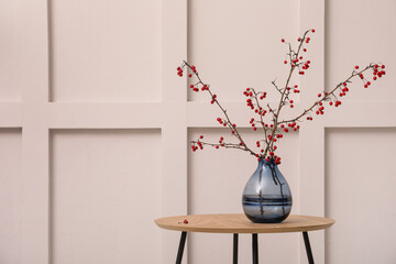 Hawthorn branches with red berries in vase on wooden table near white wall indoors, space for text. Interior element