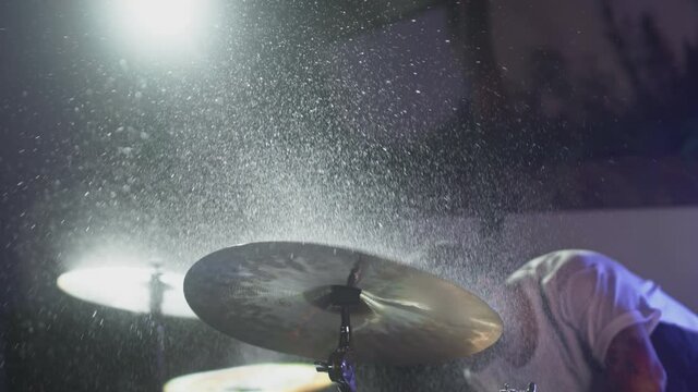 The drummer hits the wet drum cymbal with his drumstick and the water splashes in slow motion. In the recording studio of musical instruments. Knocks and beats, Repetition of rock music band.