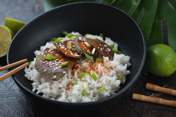 Close-up of a black bowl with white rice and slices of smoked tuna fillet, horizontal shot