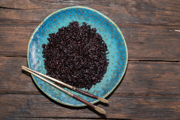 Healthy food black rice in blue plate on wood background.