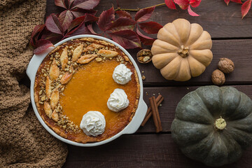 homemade pumpkin pie with walnuts and whipped cream, beautifully decorated with dough leaves, dark wooden background, top view from above