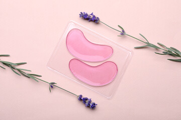 Package with under eye patches and lavender flowers on light pink background, flat lay. Cosmetic...