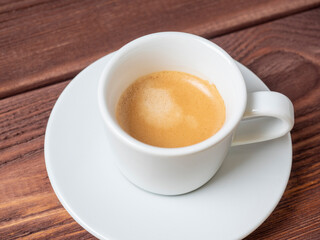 a white coffee mug with a full espresso is set on a saucer and on a wooden background. Coffee, energy drink. Delicious foam