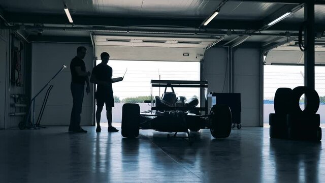 Two professionals are looking at the racing car in the workshop