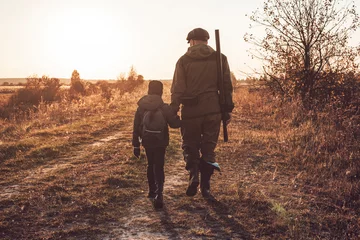  Conceptual image of a man with a shotgun walking with his son while hunting. Duck hunting season. © andy_gin