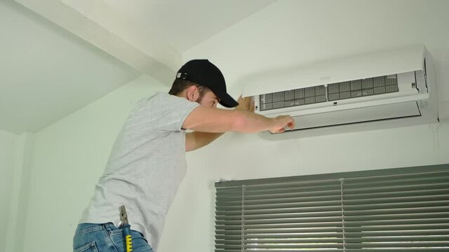 handsome young man electrician cleaning air filter on an indoor unit of air conditioning system in client house