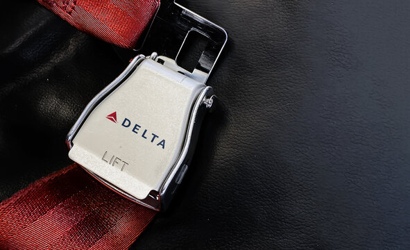 Red Lap Belt Of An Empty Seat Inside An Airplane With The Delta Airlines Logo Printed On The Metal.