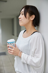 コーヒーの紙コップを持ったアジア人女性